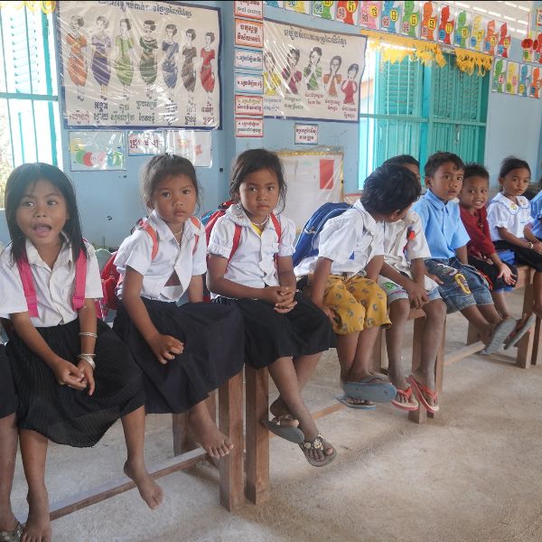 Kindergarten children in school uniform sit in a row on a wooden bench in their classroom