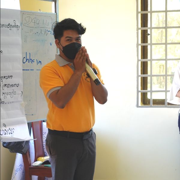A TukTuk staff member in an orange polo shirt greets the workshop with hands pressed together