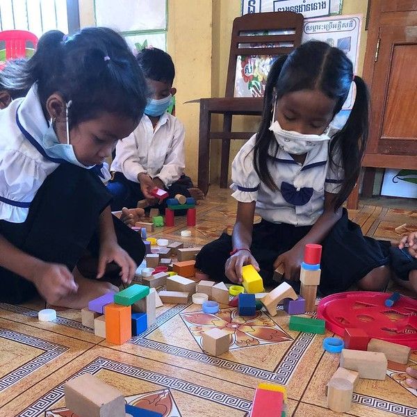 Two girls in school uniform build with wooden blocks on the classroom floor during mobile library play