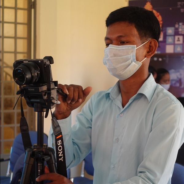 A TukTuk staff member in a face mask films a workshop with a camera on a tripod