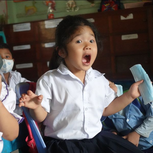 A girl in school uniform opens her mouth in surprise while holding her face mask