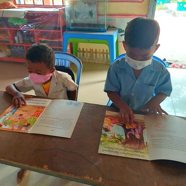Two boys look through colourful picture books at a table in a classroom