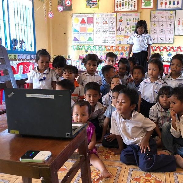 Children sit on the classroom floor and watch a laptop screen together