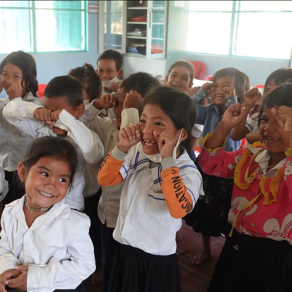 Delighted girls in school uniform smile and playfully cover their cheeks in class