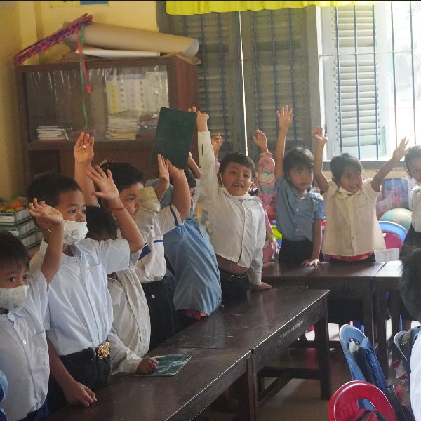 Kindergarten children in a classroom raise their hands to answer a question