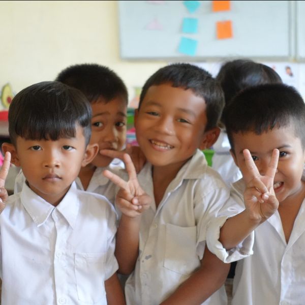 Four smiling boys in school uniform pose for the camera, two making peace signs