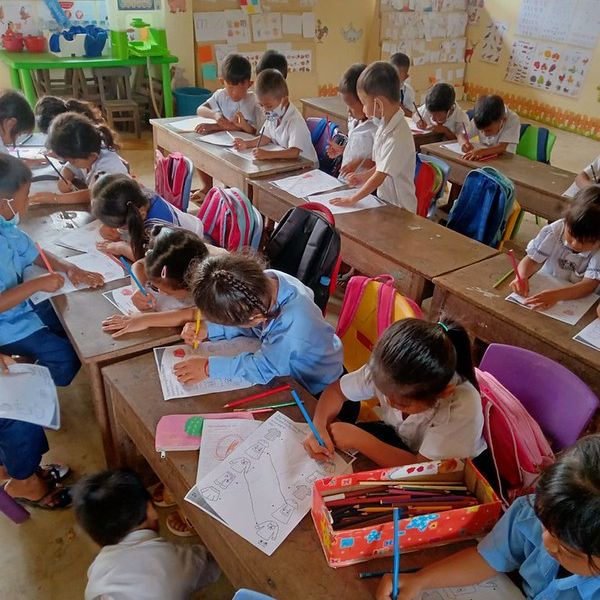 Children draw and colour on worksheets at wooden desks in a busy classroom