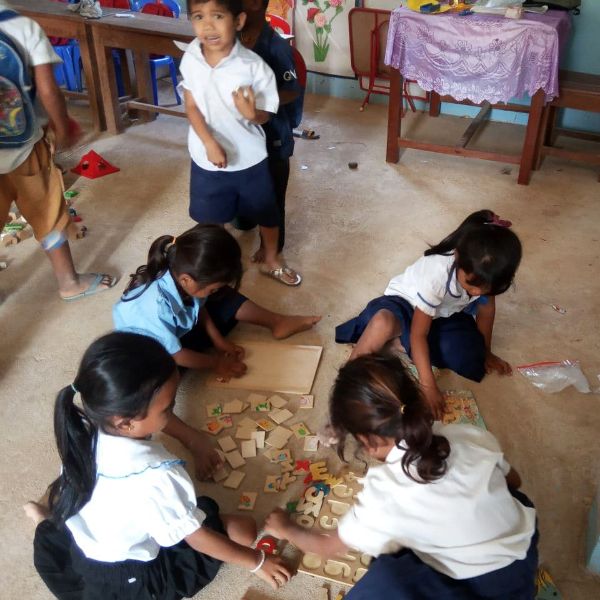 Children in school uniform kneel on a classroom floor and play together with wooden tile puzzles