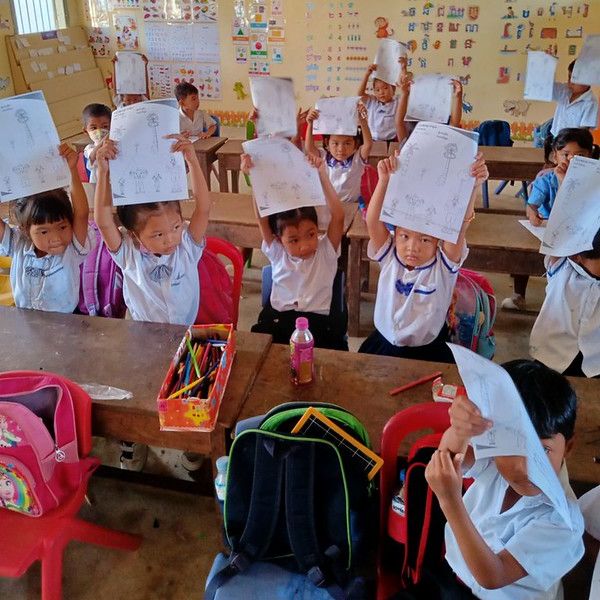 Children in a classroom hold their worksheets above their heads to show them off