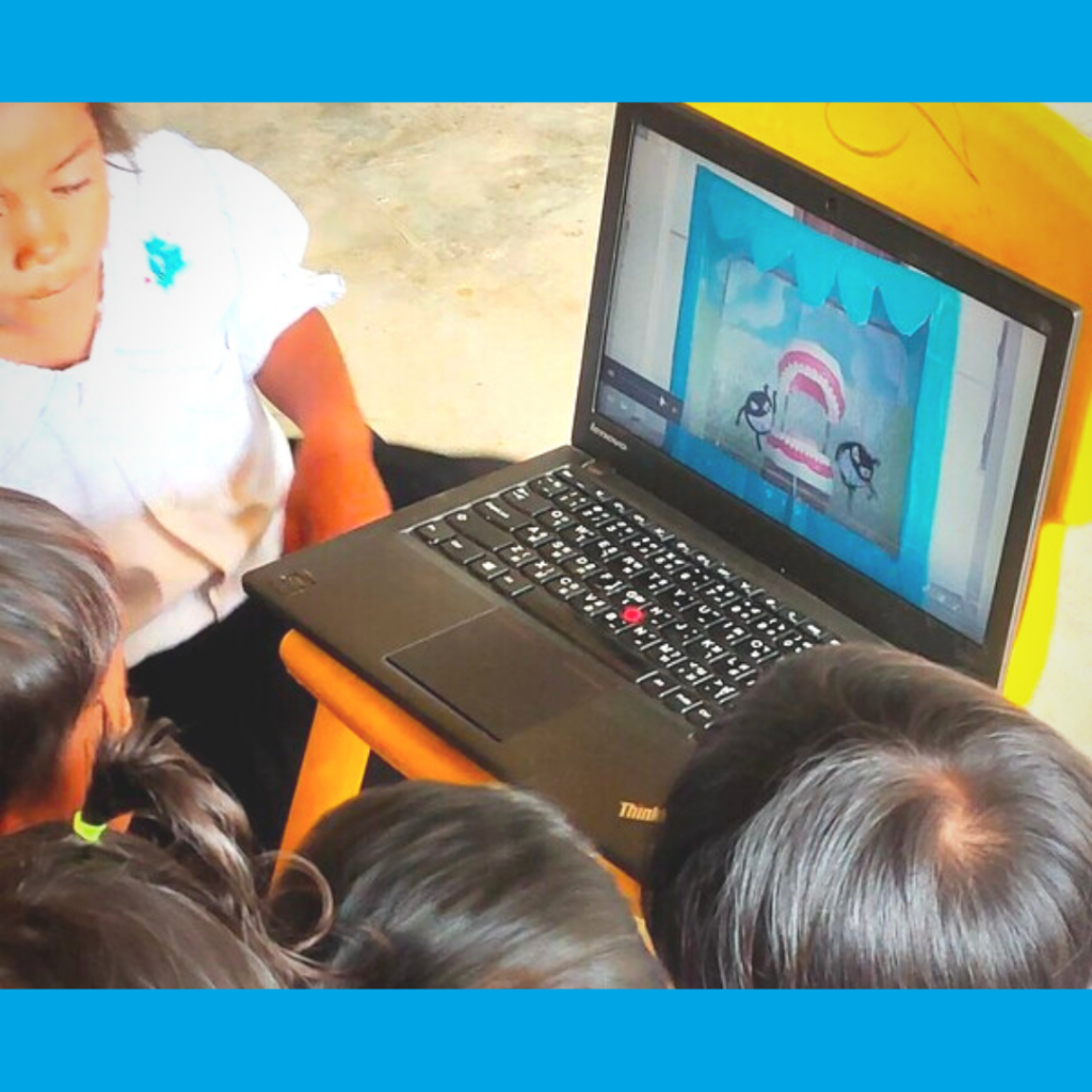 Children crowd around a laptop to watch an animated video in class
