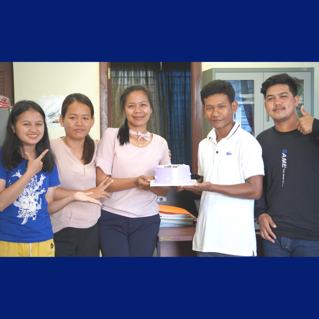 TukTuk staff and a teacher pose together in an office, holding a small cake