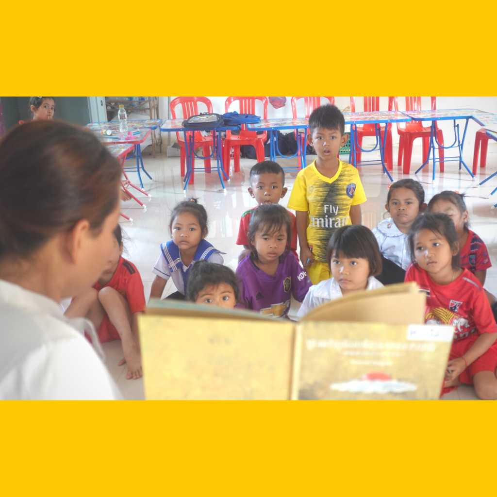 A teacher reads a large picture book to children sitting close together on the classroom floor