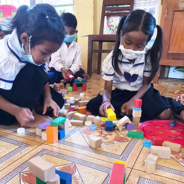 Two girls in school uniform build with wooden blocks on a classroom floor