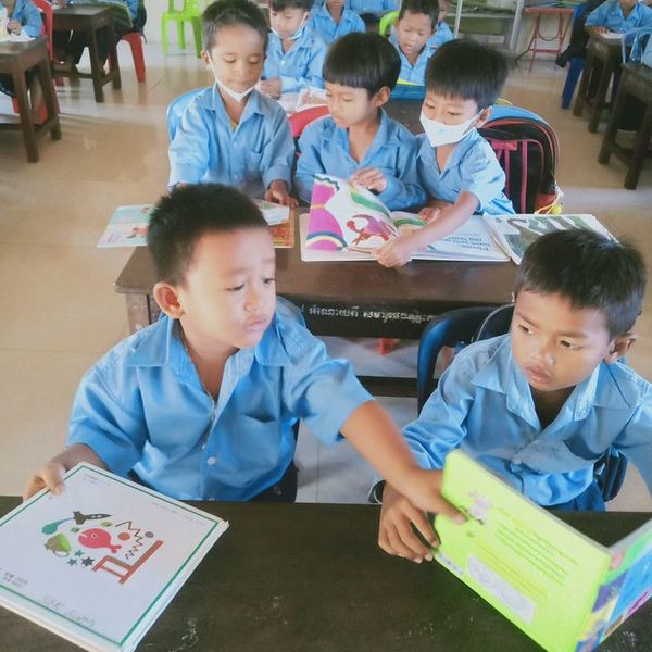 Two boys in blue uniforms share picture books at their desks in a classroom