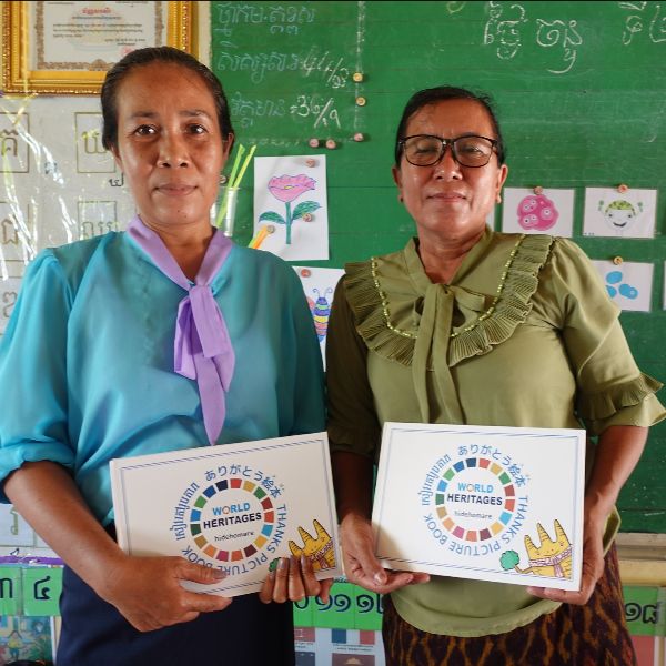 Two teachers stand in a classroom, each holding a World Heritages thank-you picture book