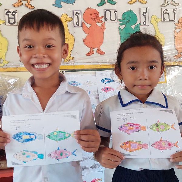 A boy and a girl proudly hold up their coloured fish worksheets in a classroom