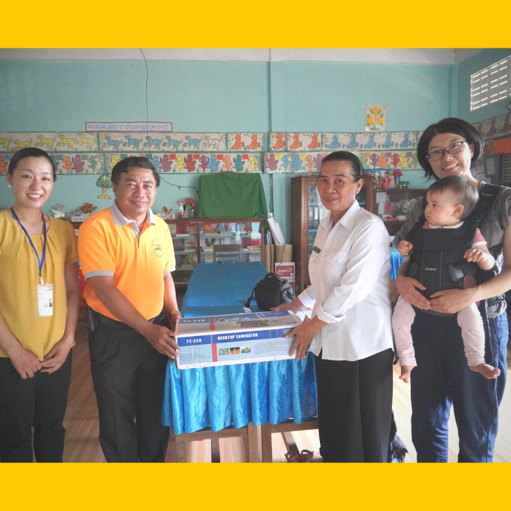 TukTuk staff and a school staff member pose with a boxed donation of equipment in a classroom