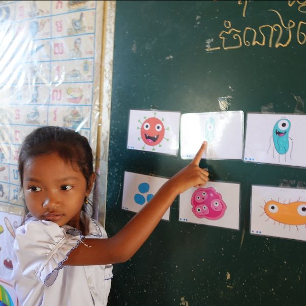 A girl points to cartoon germ picture cards on a classroom board