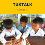 Three boys, two in white shirts and one in light blue, look through a picture book together