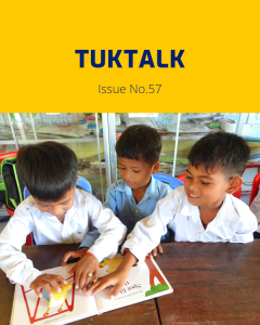 Three boys, two in white shirts and one in light blue, look through a picture book together