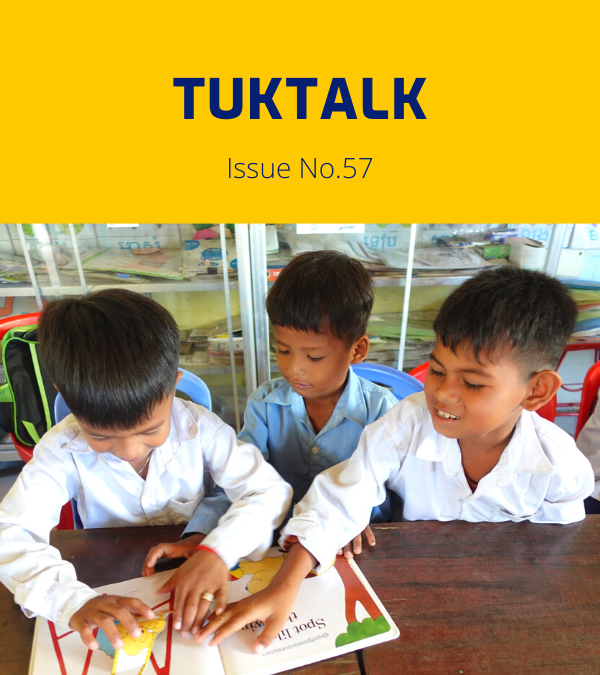 Three boys, two in white shirts and one in light blue, look through a picture book together