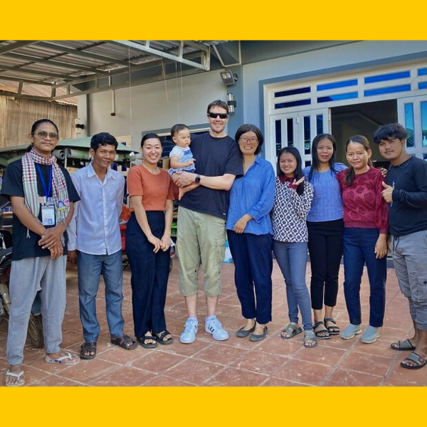 TukTuk staff, visiting volunteers and a baby stand in a row outside a building