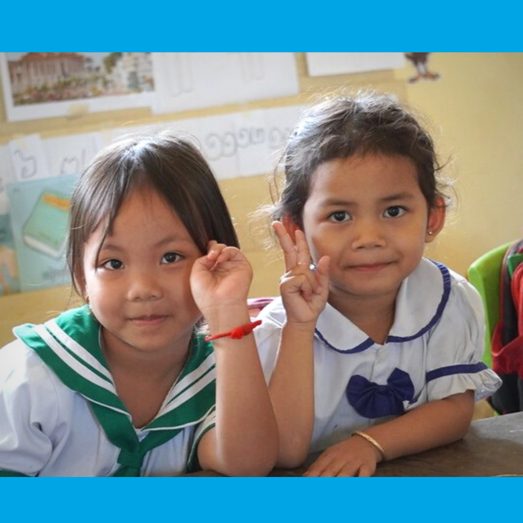 Two girls in school uniform smile and make peace signs at a desk