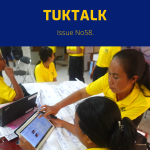 Teachers in yellow shirts use a tablet and laptop around workshop flip charts