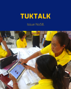 Teachers in yellow shirts use a tablet and laptop around workshop flip charts