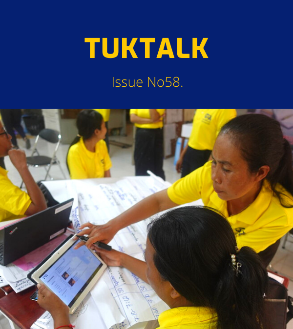 Teachers in yellow shirts use a tablet and laptop around workshop flip charts