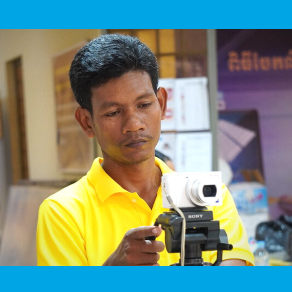 A TukTuk staff member in a yellow shirt films the workshop with a camera on a tripod
