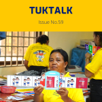 A teacher in a yellow shirt holds up a strip of decorative classroom cards
