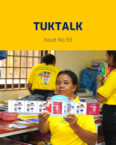 A teacher in a yellow shirt holds up a strip of decorative classroom cards