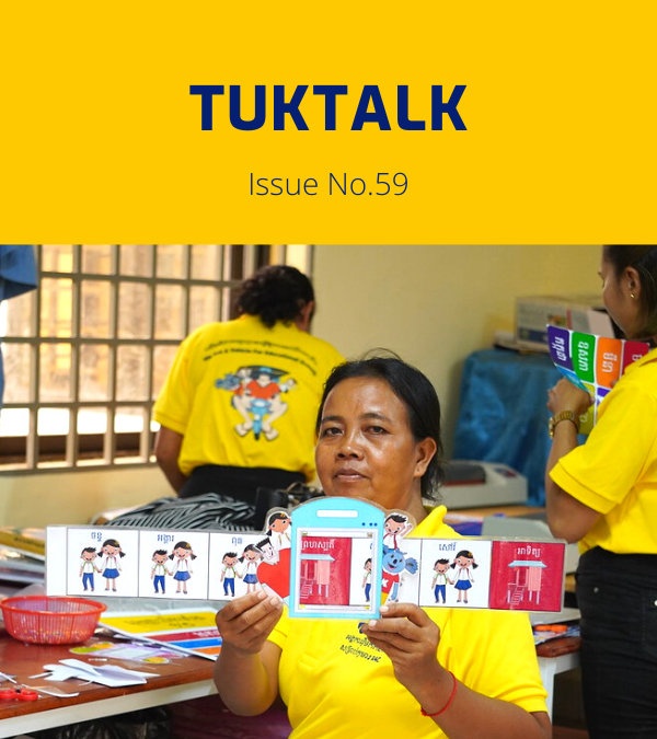 A teacher in a yellow shirt holds up a strip of decorative classroom cards