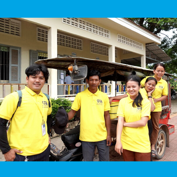 TukTuk staff in yellow shirts pose in front of a school building next to a tuk-tuk