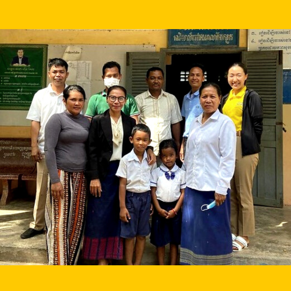 TukTuk staff, teachers and children pose together in front of a school door