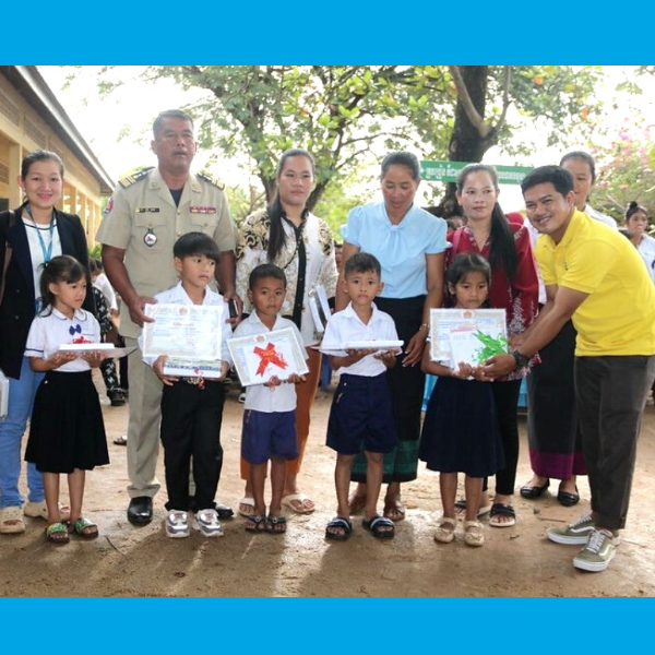Children hold certificates and paper crafts, standing with teachers, an official and a TukTuk staff member