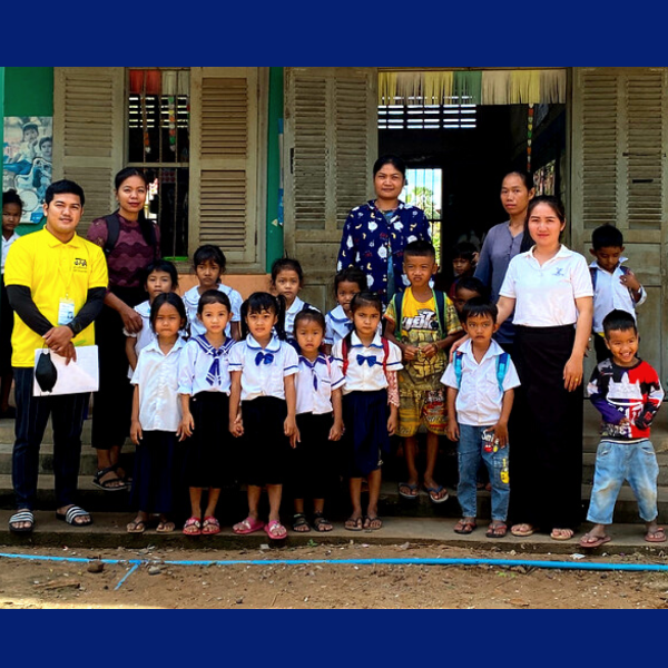 A TukTuk staff member, a teacher and children in school uniform pose in front of a classroom