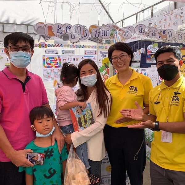 TukTuk staff pose with visiting families at the Cambodia Book Fair booth hung with classroom decorations