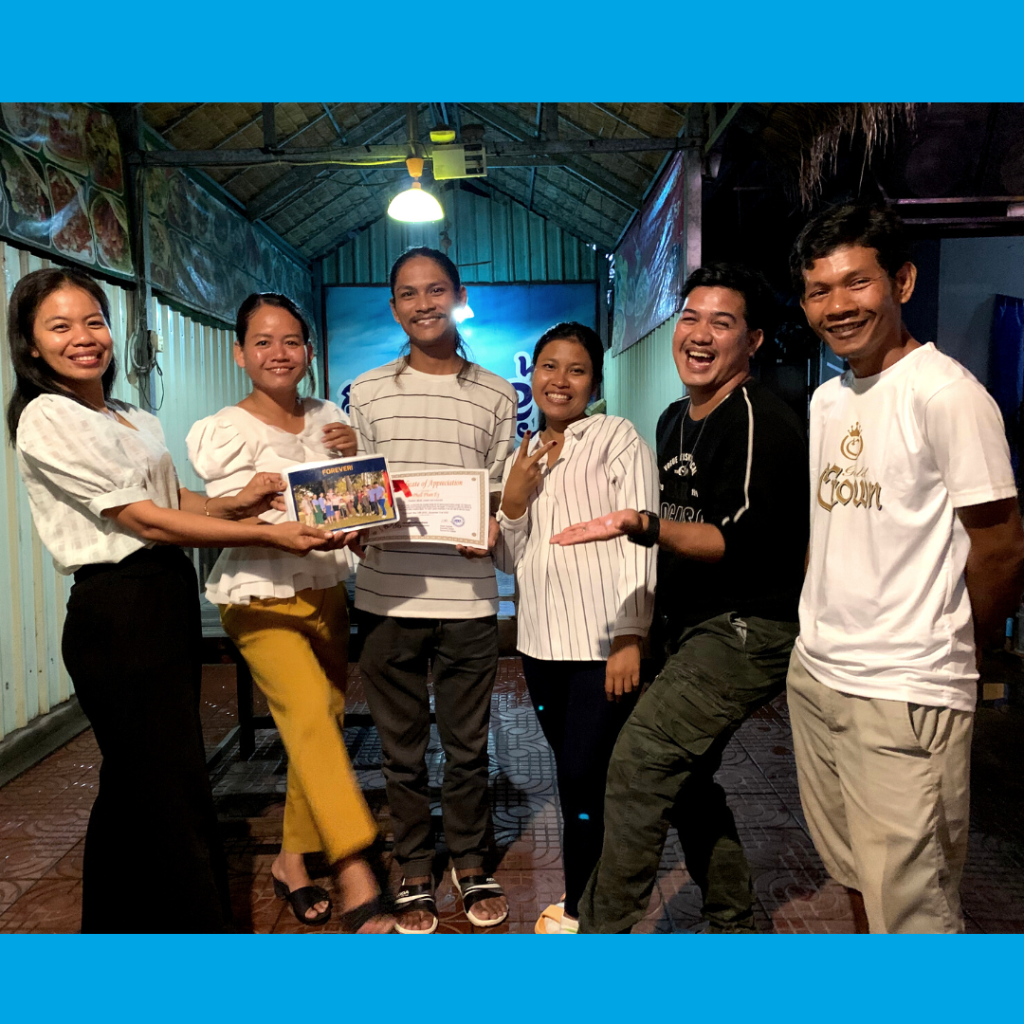 Six TukTuk staff pose together at the evening party, presenting a certificate and a small gift