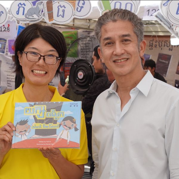 A TukTuk staff member holds the picture book Jack the Giant beside a smiling visitor at the book fair