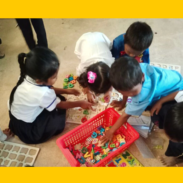 Children sit on the floor playing with a basket of wooden letters and a letter puzzle