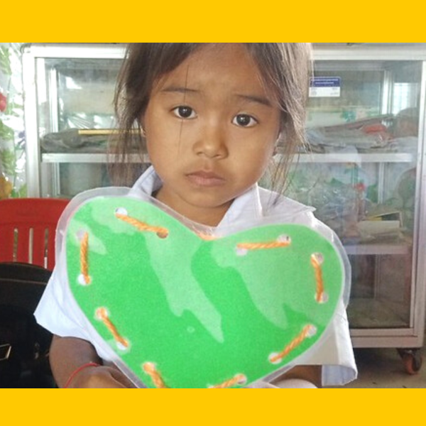 A girl in school uniform holds up a green heart-shaped lacing card