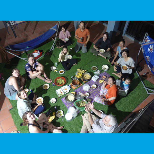 Voluntukers and TukTuk staff share a picnic meal on artificial grass, seen from above