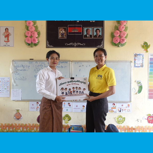 A TukTuk staff member and a teacher hold a new picture book together in a decorated classroom