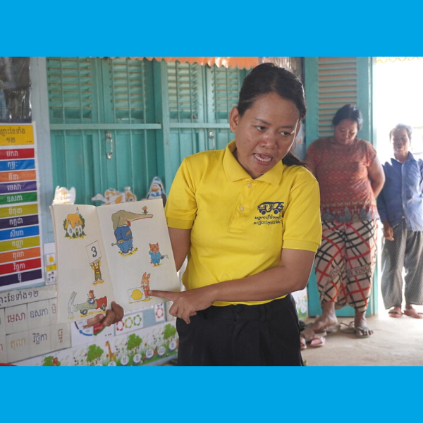 A TukTuk staff member shows a page of a picture book to teachers in a classroom doorway