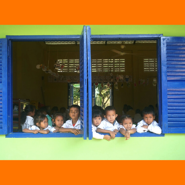 Preschool children in school uniforms lean out of a blue classroom window