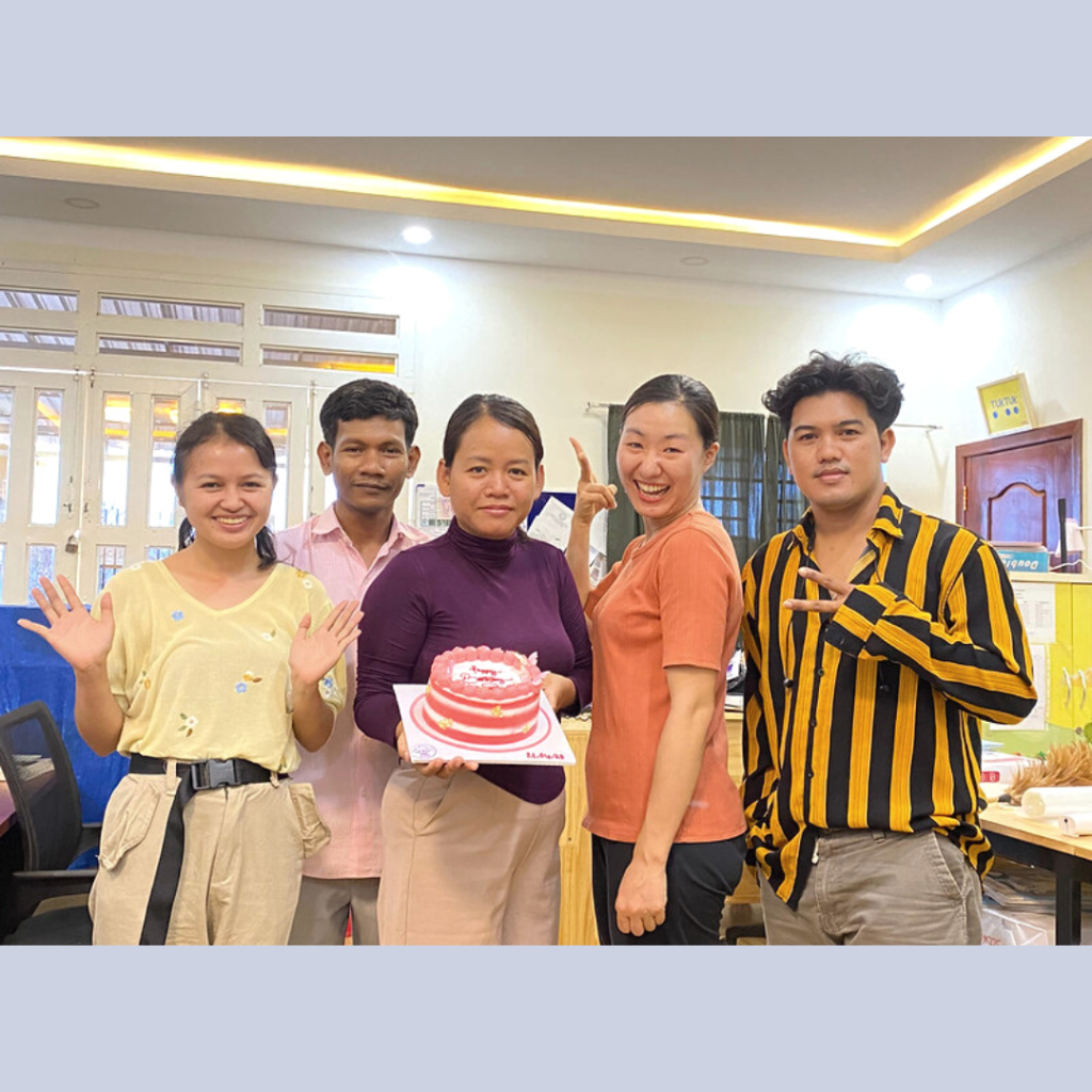 TukTuk staff gather in the office holding a birthday cake and waving at the camera