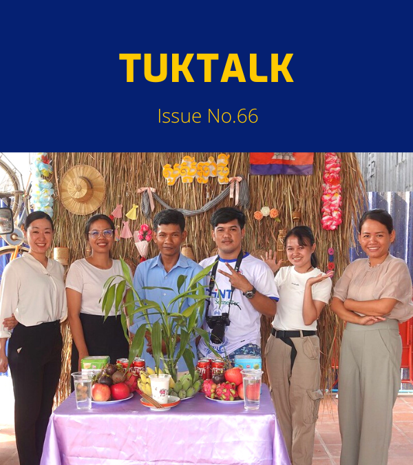 TukTalk 66 cover: TukTuk staff and visitors pose behind a table of fruit in front of a straw wall