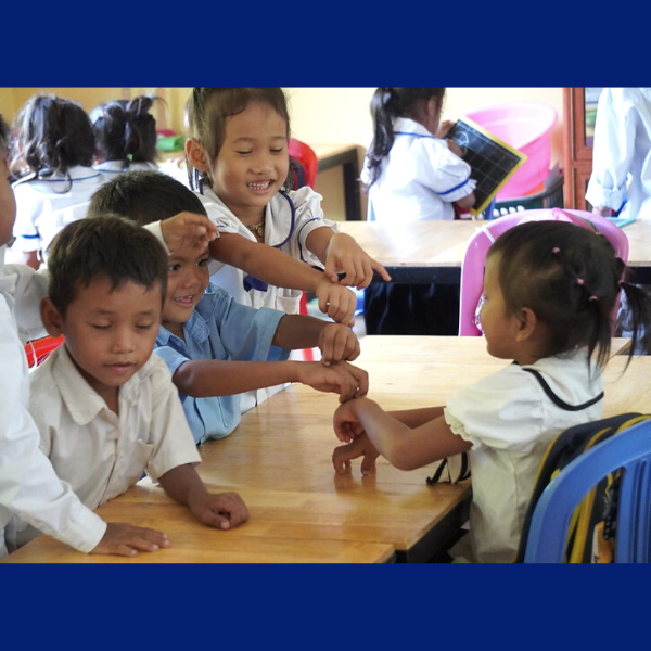 Four preschool children at a wooden table in class stretch out their arms and look at each other's hands